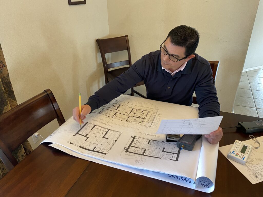Dr. Carlos Loredo Ritter is analyzing the last readings from an EMF Home Assessment by using equations and making notes in the floor plan of the house